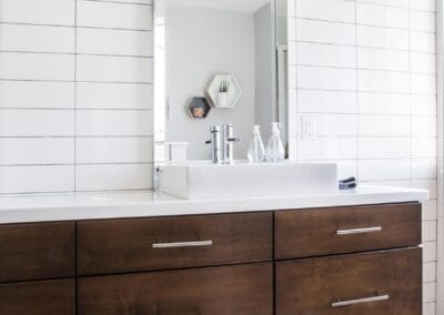 A beautifully custom-built bathroom with white tiles, and brown furniture. This bathroom also features dark grey floor tiling in the shape of hexagons.