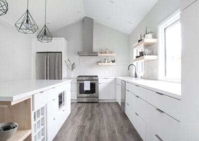 A chic custom built home featuring cool wood floors and white walls for contrast. This home has an open concept floor plan between the kitchen and living room. The kitchen features open shelving, and modern style drawers.