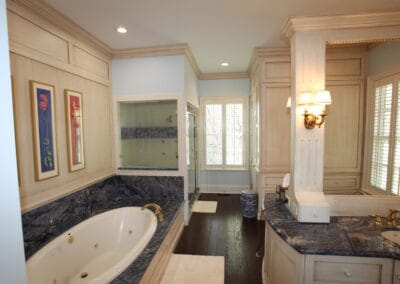 A master bathroom featuring cool toned, granite counters and dark wood floors. This bathroom also has a custom shower and a jacuzzi tub.