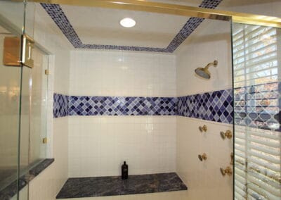 a custom built shower with a granite bench and blue accent stones in the walls and ceiling.