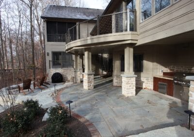 A custom built two story deck and patio. The patio features cool toned stone flooring and a built in grill with counters. Also included is a bonfire set up with a view.