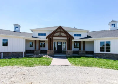 A white farmhouse with white wainscoting exterior, and brown columns leading to the front door.