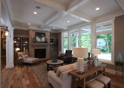 A timeless living room with an open concept. This living room features a box beam (coffered) ceiling, a brick fireplace, and brown wooden floors.