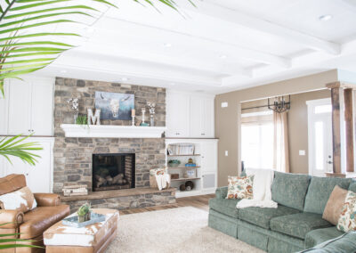 A living room featuring a tan accent wall, white cabinets, a green couch and a tan leather chair.