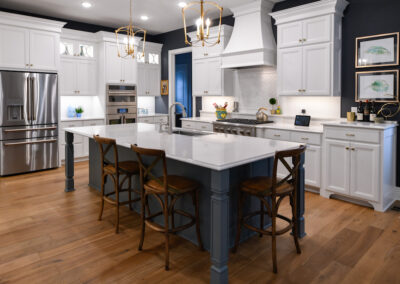 A modern kitchen featuring contrasting colors with white cabinets, white countertops, and charcoal blue kitchen island.