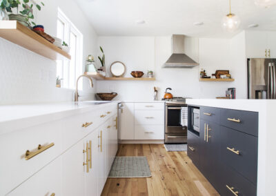 A modern kitchen with white kitchen cabinets, charcoal kitchen island, and floating shelves.