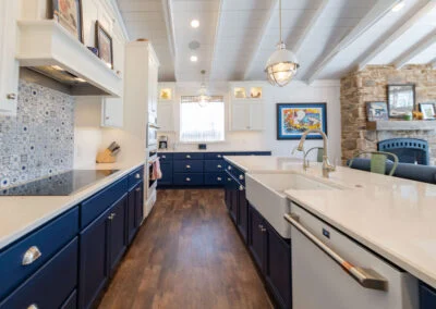 A white kitchen featuring white top cabinets and blue bottom cabinets. Hardware on the cabinets are brushed nickel. This kitchen also features a blue and white patterned backsplash behind a countertop stove.