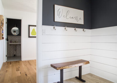A foyer with white shiplap walls, and a rustic wooden bench.