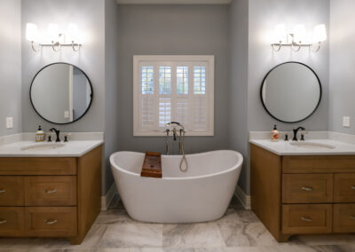 A custom symmetrical bathroom with Jack & Jill sinks, separated by a standalone porcelain tub.