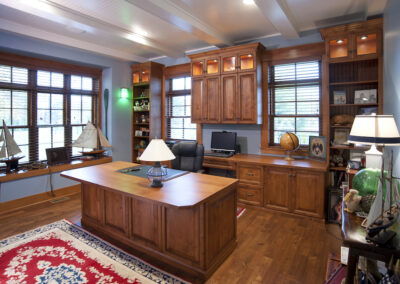 Custom built office with built in bookshelves, and cabinets. There is a wooden work desk in the middle of the room