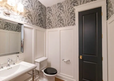 A black and white style bathroom with white panelling, and a wallpaper with a feathered design.