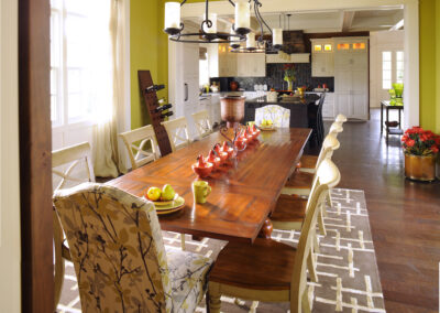 A chartreuse colored dining room with a long woodern table. The dining room leads into a kitchen with black backsplash, a black kitchen island and contrasting white cabinets.