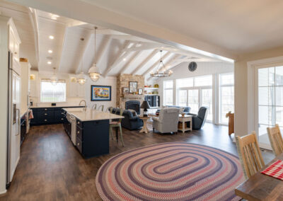 An open concept kitchen and diningroom with vaulted ceilings, black bottom cabinets, and white top cabinets. The dining room features a soft red, purple, and white oval rug.