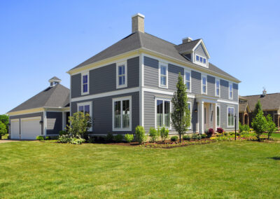 an exterior of a home with grey green siding, white window frames, and columns on each side of the front door.