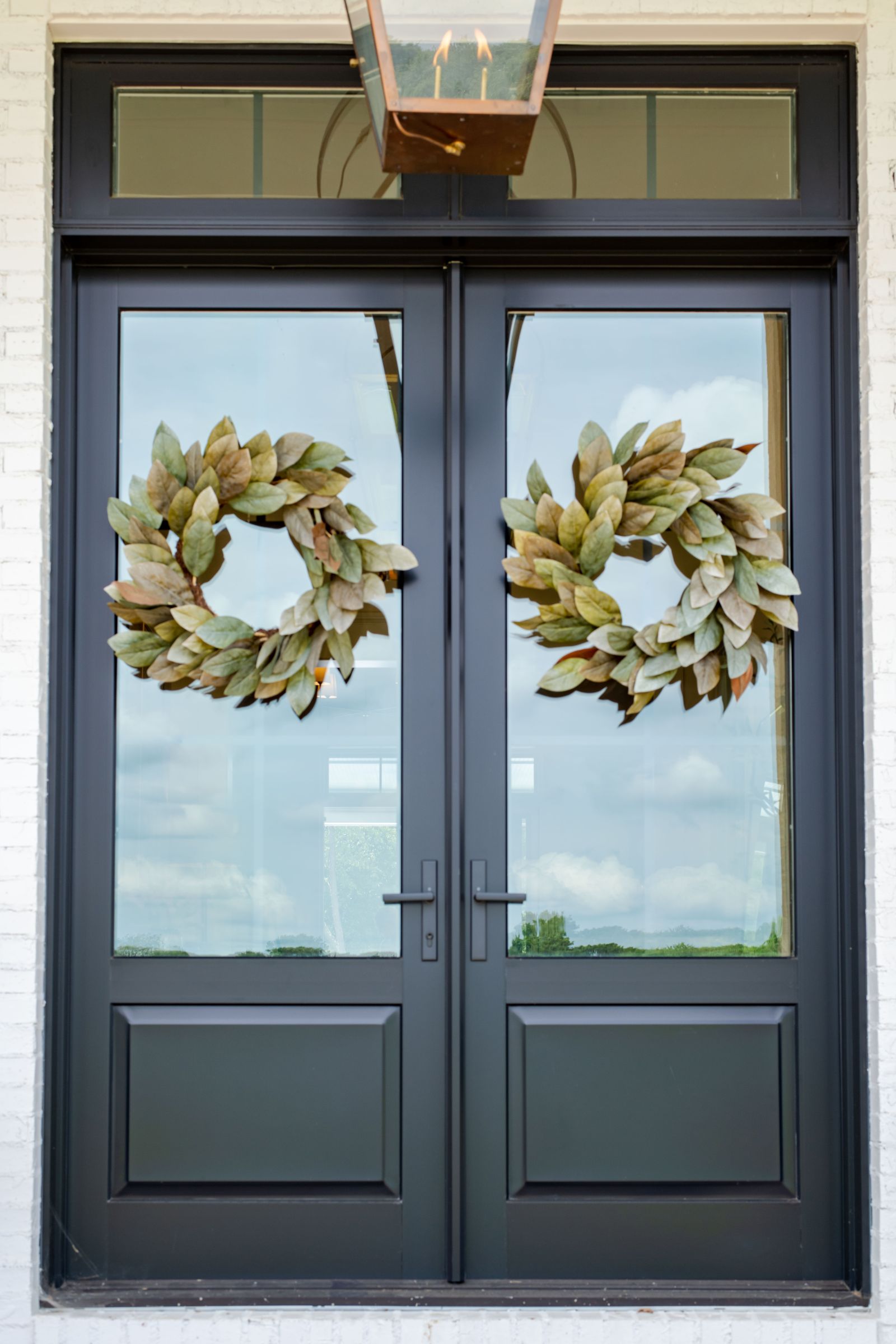 A dark gray french door with glass windows and a a green leafy wreath over both doors.